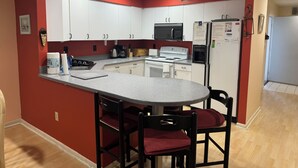 A compact kitchen with white cabinets, a microwave, a refrigerator, and a small dining area with two chairs. - Ground Level Condo 3 Community Pools and Tennis (Rehoboth Beach)