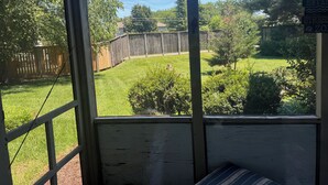 A view through a window of a backyard with a wooden fence, trees, and a grassy area. - Ground Level Condo 3 Community Pools and Tennis (Rehoboth Beach)