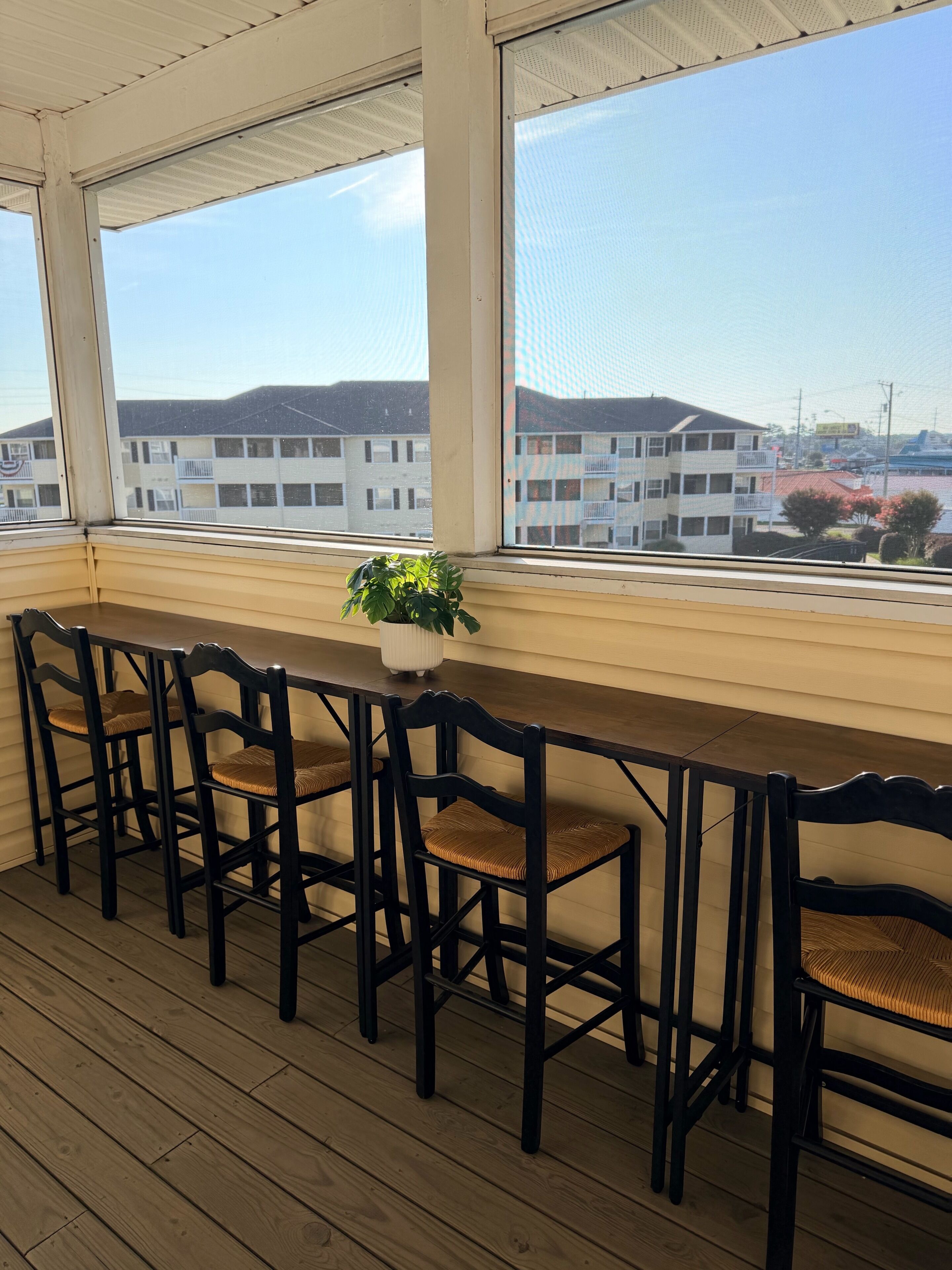 A covered outdoor seating area with a wooden floor, a long table, and four chairs.