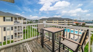 A balcony with a table and chairs, overlooking a swimming pool and adjacent buildings. - Linens Supplied Rehoboth Beach Condo Walk to Shops and Restaurants (Rehoboth Beach)