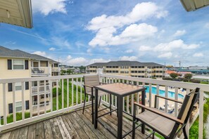 Ein Balkon mit Tisch und Stühlen, mit Blick auf einen Swimmingpool und angrenzende Gebäude.
