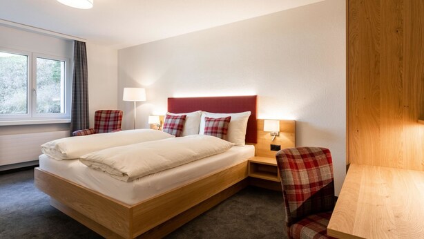 A hotel room with a bed, two bedside tables, a chair, a desk, and a window. - Chalchboda 1 Appartement/Fewo, Dusche und Bad, WC, 7-Bettwohnung by Interhome (Arosa)