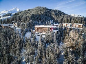 Ein schneebedecktes Bergresort mit mehreren Gebäuden, darunter ein großes Hotel mit Balkonen.