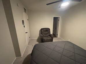 A bedroom with a bed, a recliner, a door, and a ceiling fan. - Fairview Hideaway - 3BR Near U of A & Downtown + EV Charger (Tucson)