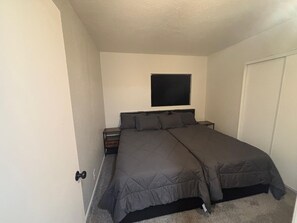 A bedroom with a bed, a nightstand, a window, and a door. - Fairview Hideaway - 3BR Near U of A & Downtown + EV Charger (Tucson)