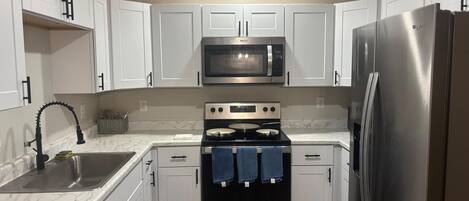 A modern kitchen with white cabinets, a stainless steel refrigerator, a microwave, an oven, and a dishwasher.