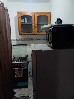 Een kleine keuken met een fornuis, magnetron en een houten kastje.
