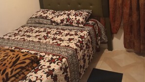 Ein Schlafzimmer mit einer gesteppten Kopfteil, einem Bett mit gemusterten Bettbezügen, einer Leopardenfell-Decke und einem Fenster mit aufwendigen Vorhängen.