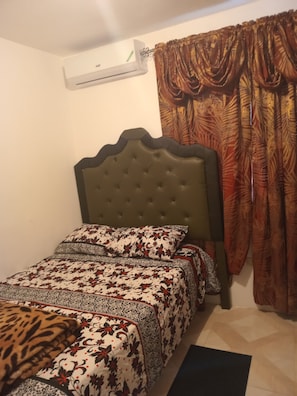 Ein Schlafzimmer mit einer gesteppten Kopfteil, einem Bett mit gemusterten Bettbezügen, einer Leopardenfell-Decke und einem Fenster mit aufwendigen Vorhängen.