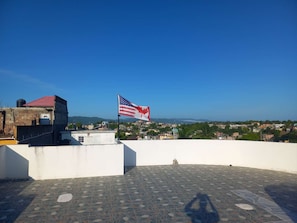 Eine Dachterrasse mit einer Flagge, Blick auf eine Stadtlandschaft und einem gefliesten Boden.