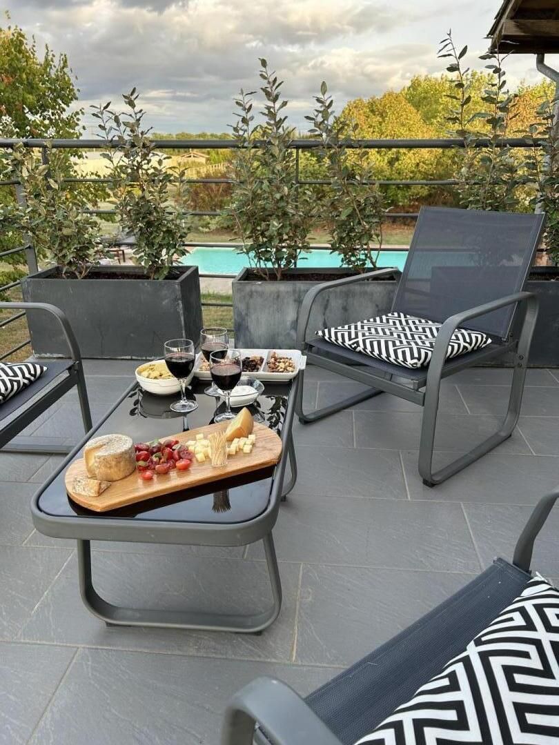 Une terrasse extérieure avec une table dressée pour un repas, des chaises dotées de coussins à motifs et une vue sur une piscine.