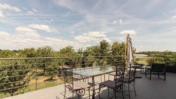 Een glazen tafel met metalen stoelen en een parasol op een balkon met een metalen hekwerk.