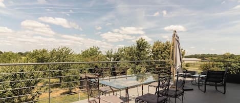 Ein Tisch mit Glasplatte, Metallstühle und Sonnenschirm auf einem Balkon mit Metallgeländer.