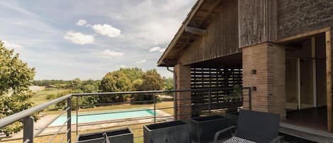 A balcony with outdoor seating, a pool, and a view of the surrounding landscape.