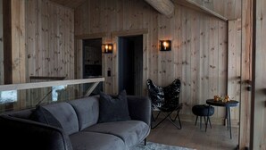Een houten interieur met een bank, een stoel, een klein tafeltje en twee wandlampen.