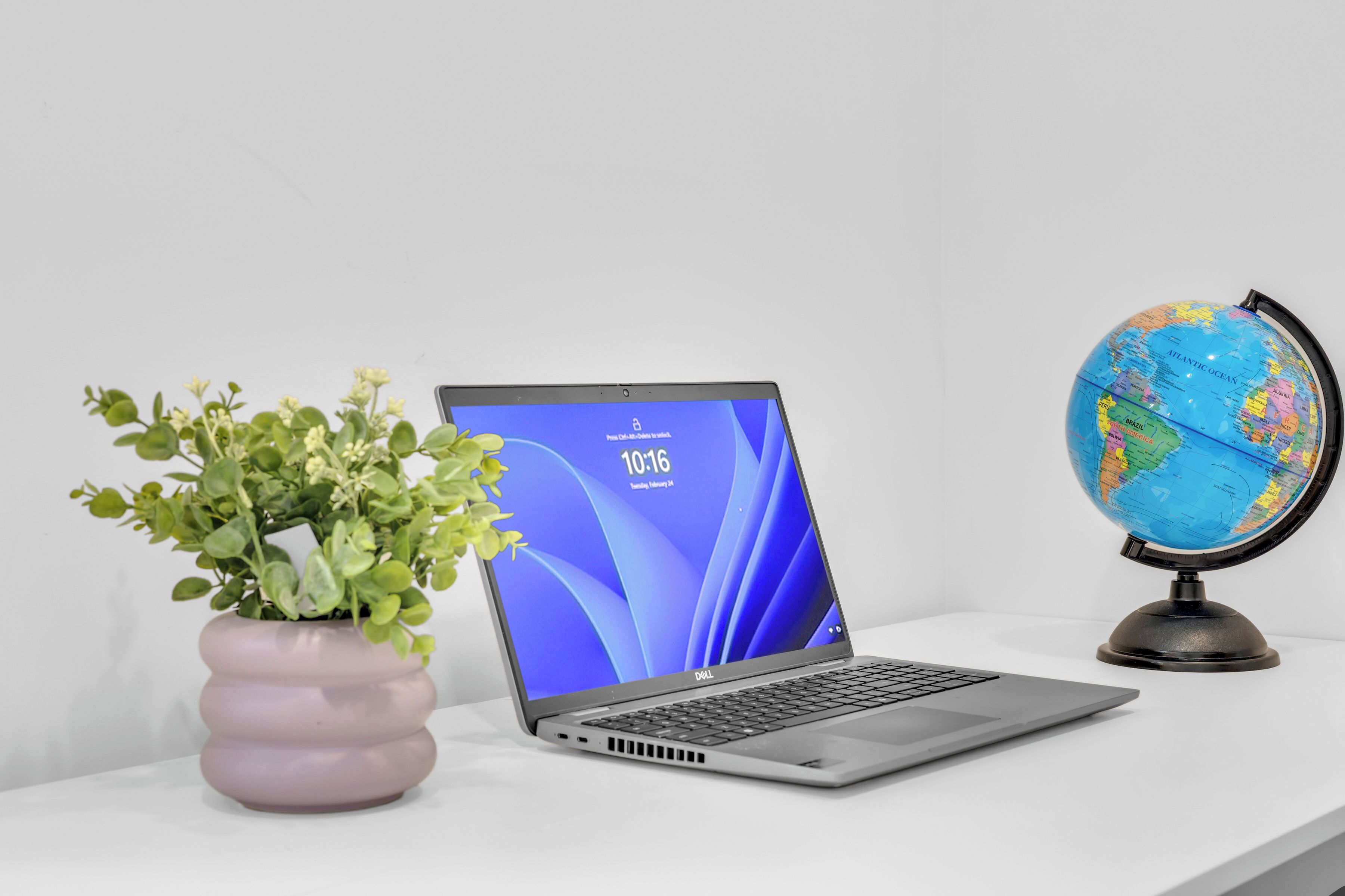 A laptop on a white surface with a globe and a potted plant beside it.