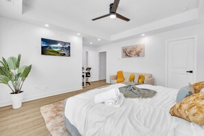 Een moderne slaapkamer met een bed, een bureau, een stoel, een plafondventilator en een groot raam.