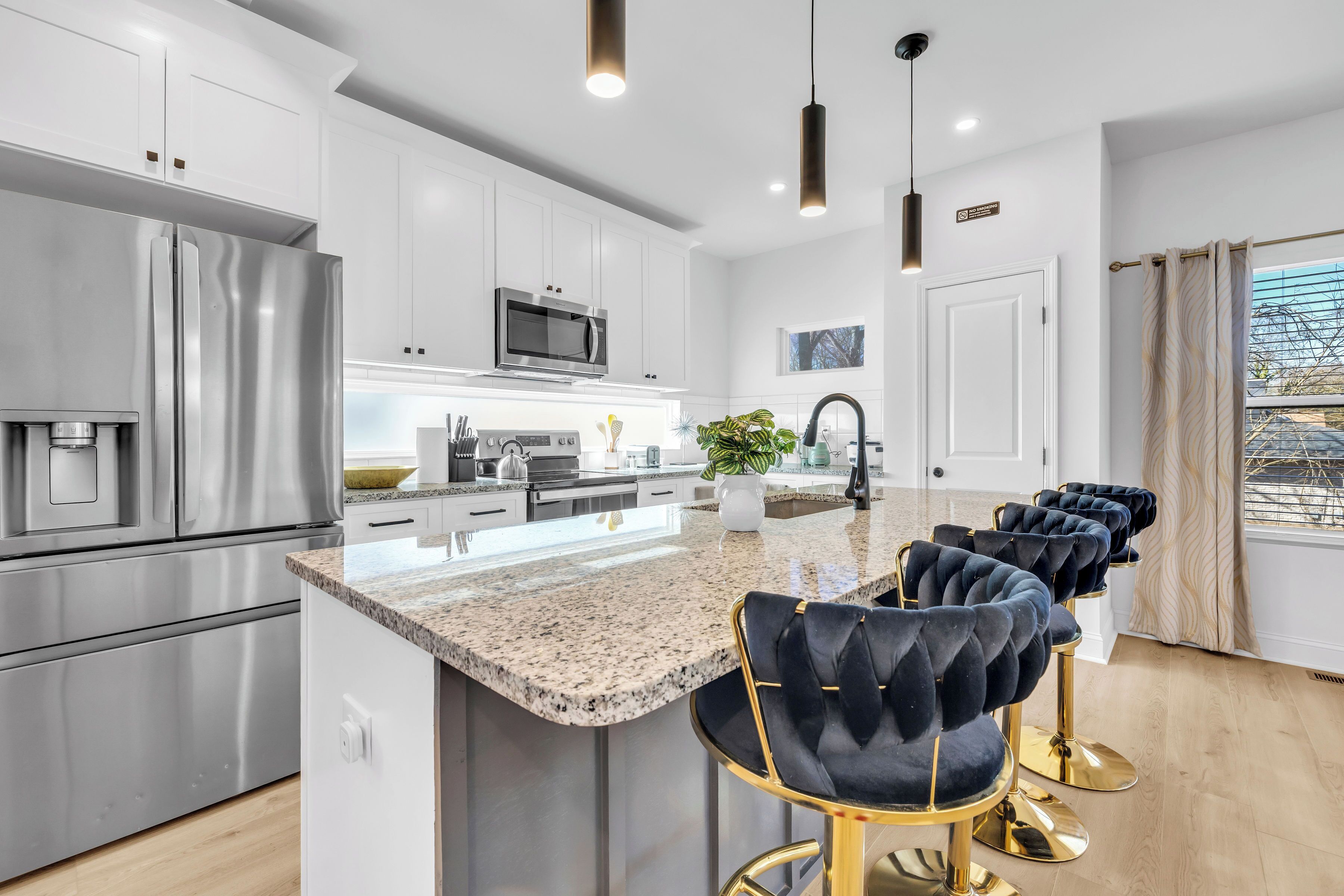 A modern kitchen with stainless steel appliances, a granite countertop, and a bar area with velvet barstools.