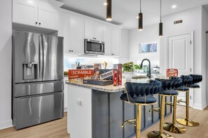 A modern kitchen with stainless steel appliances, white cabinets, and a bar area with velvet barstools. - New! Ivy Luxury Home Near Airport And Downtown (East Point)
