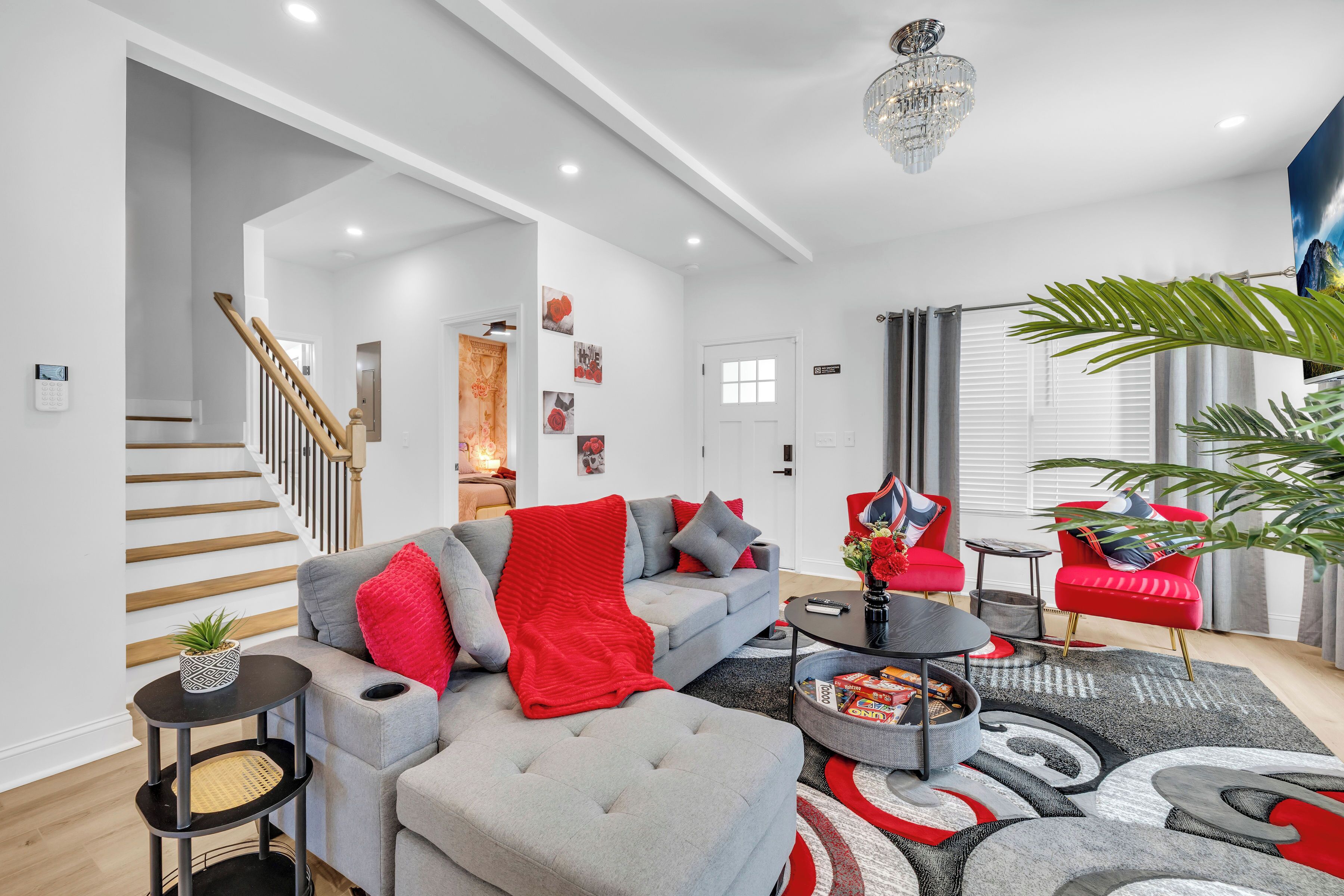 Un salon moderne avec un canapé gris, des touches de couleur rouge, un escalier et un lustre.