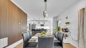 Ein moderner Essbereich mit einem langen Tisch, schwarzen Stühlen mit goldenen Akzenten und einer zentralen Leuchte.