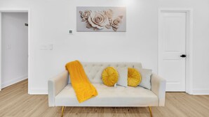 Ein weißes Sofa mit einer gelben Decke und zwei gelben Kissen, eine weiße Tür und ein Wandbild mit Blumenmotiven.