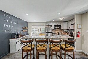 Una cocina moderna con una isla central, taburetes de bar y un letrero inspirador en la pared.