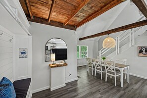 Un amplio salón con una mesa de comedor, paredes blancas, techo de madera y una escalera.