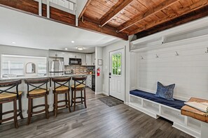 A kitchen with a central island, bar stools, and a seating area with a bench and cushions. - Soaking Bear Chalet • Hot Tub & Lake Access (Blakeslee)