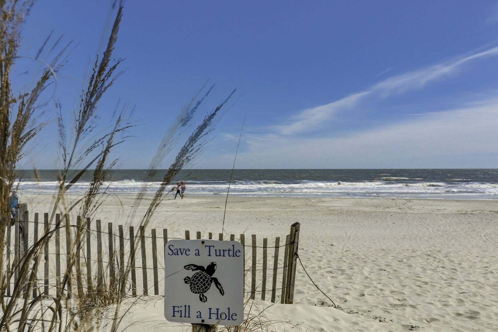 A beach with a sign that reads 'Save a Turtle Fill a Hole.'