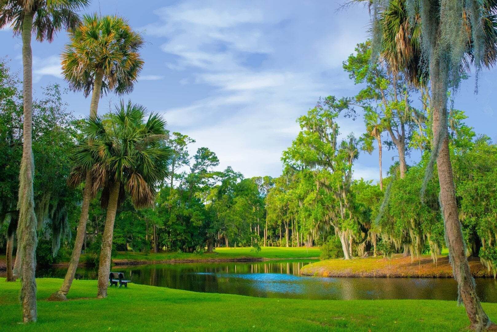 A serene golf course with a pond, surrounded by lush greenery and tall trees.