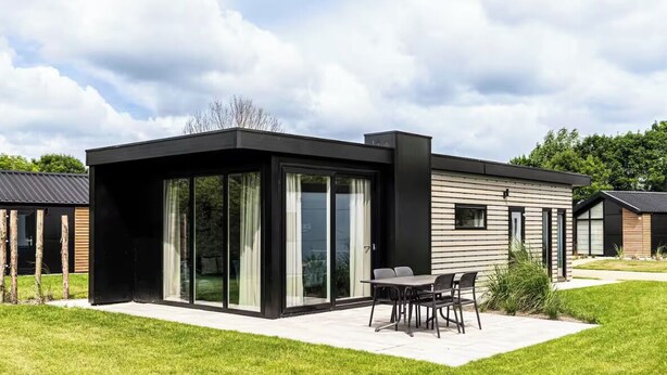 Ein modernes Haus mit Terrasse, großen Schiebegläsern und einer kleinen Sitzgelegenheit im Freien.