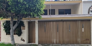 A residential building with a garage door, a tree in front, and a small window on the side.