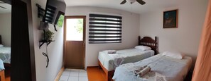 Un dormitorio con dos camas, una ventana con persianas, un ventilador de techo y un cuadro en la pared.