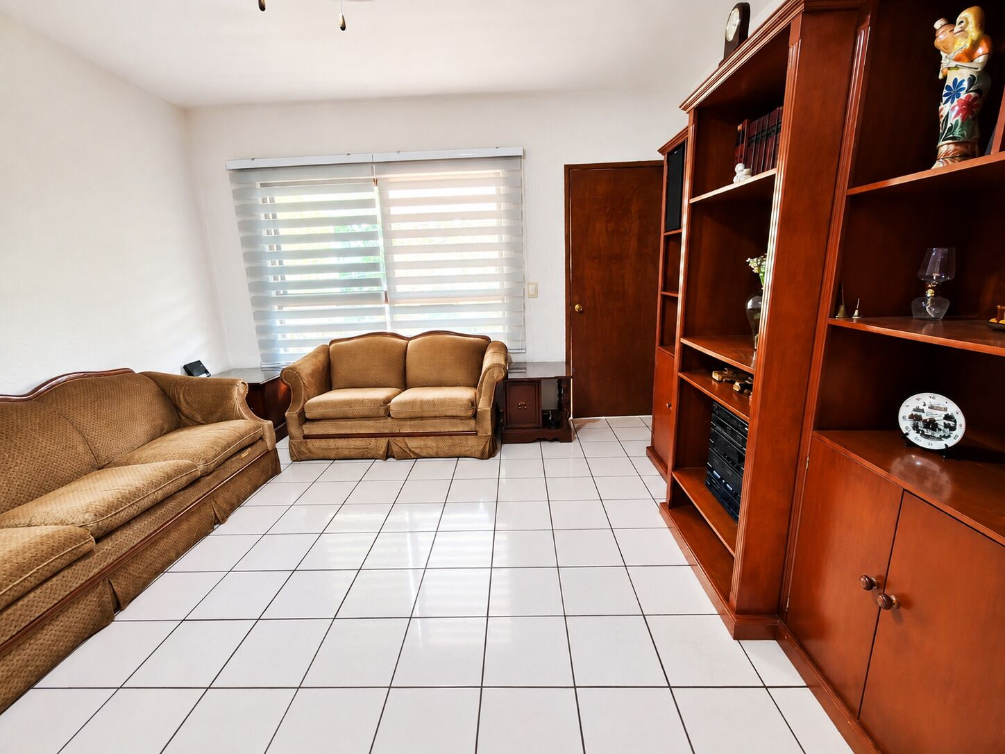 A living room with a sofa, a wooden cabinet, and a window with blinds.