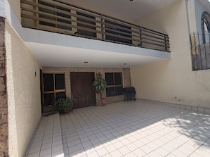 Un edificio de dos pisos con un patio empedrado, una puerta de madera y un ventanal con reja de metal.
