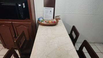 Une table à manger avec un plateau en marbre, entourée de quatre chaises, dans une pièce équipée d’un four à micro-ondes et agrémentée d’une pancarte de bienvenue.