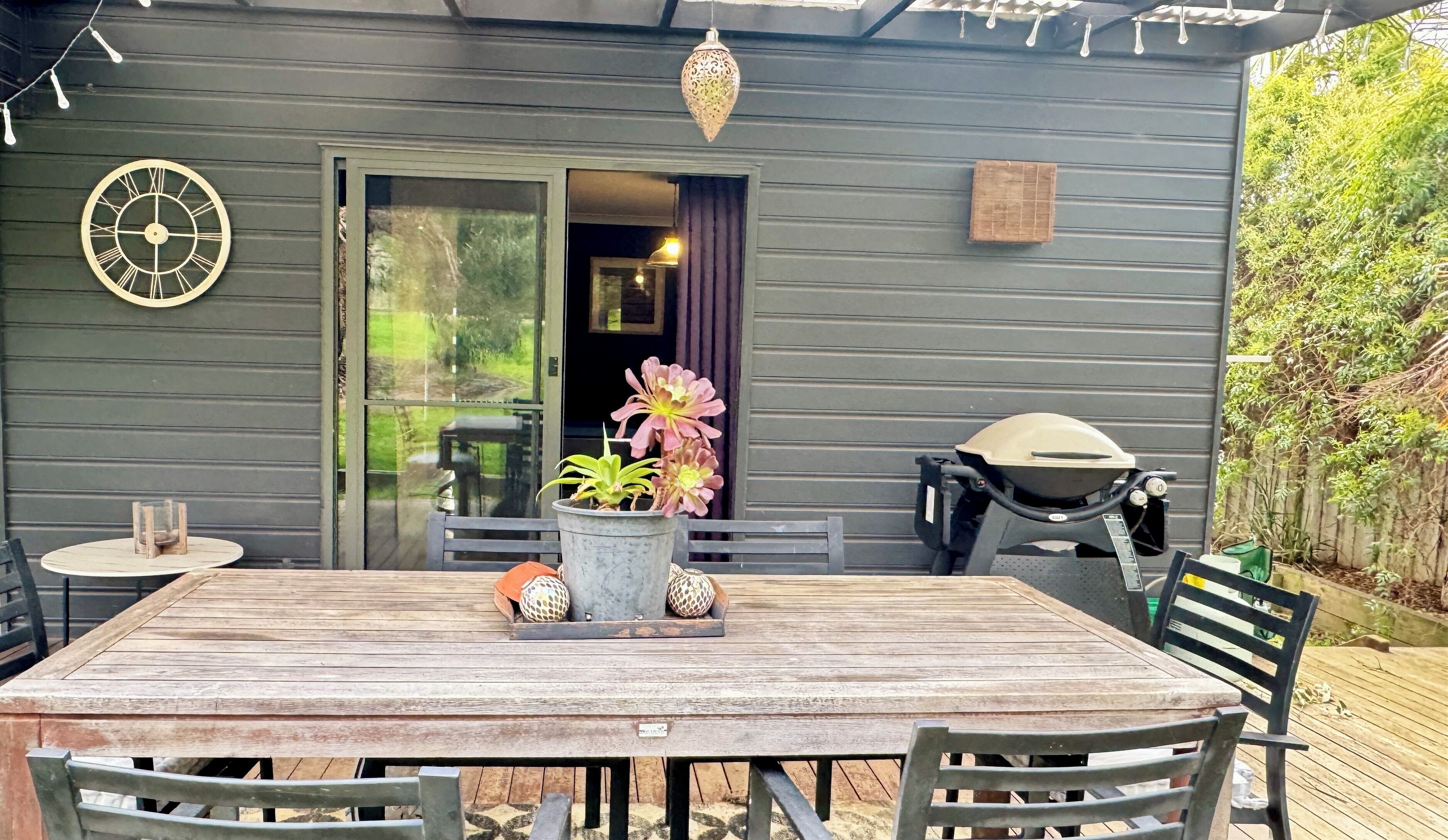 En træterrasse med et bord, stole, en potteplante, dekorative kugler, et ur og en grill.