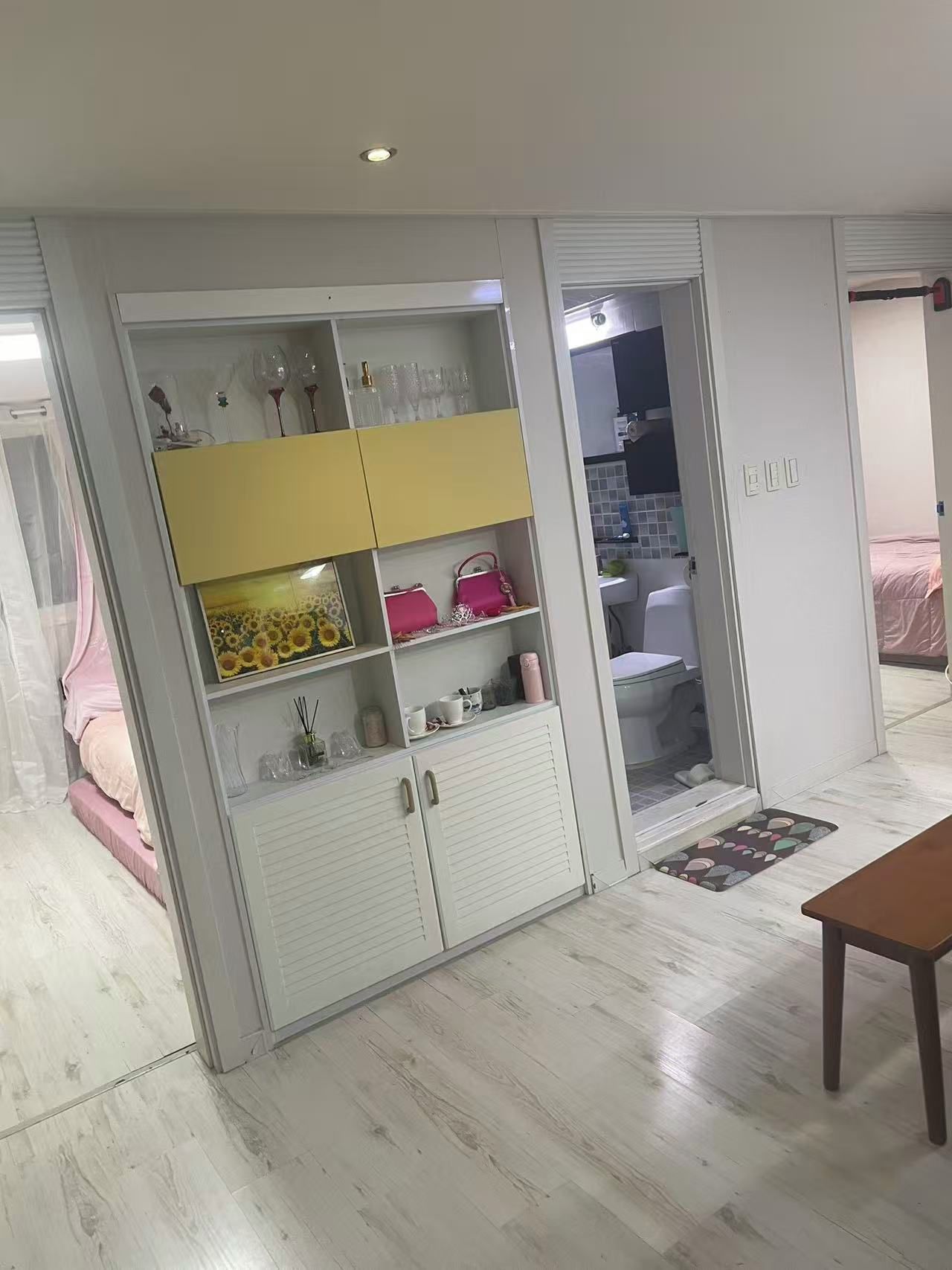 Una habitación con un armario blanco, una cama con colcha rosa y una mesa de madera.