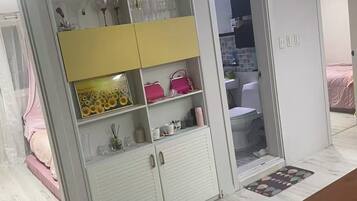 Una habitación con un armario blanco, una cama con colcha rosa y una mesa de madera.