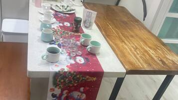 Una mesa de comedor con mantel festivo, varias tazas, un hervidor y una cafetera.