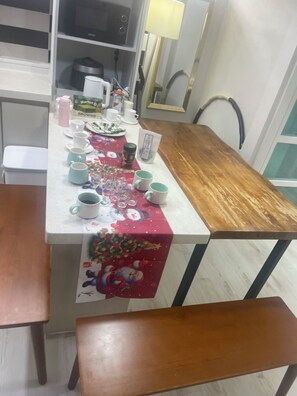 A dining table with a festive tablecloth, various cups, a kettle, and a coffee maker.