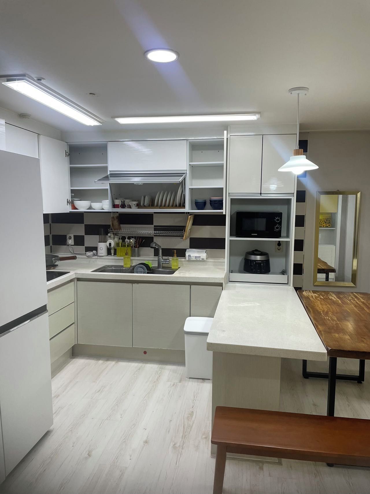 A modern kitchen with white cabinetry, a built-in microwave, and a wooden bench.