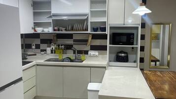 A modern kitchen with white cabinetry, a built-in microwave, and a wooden bench.