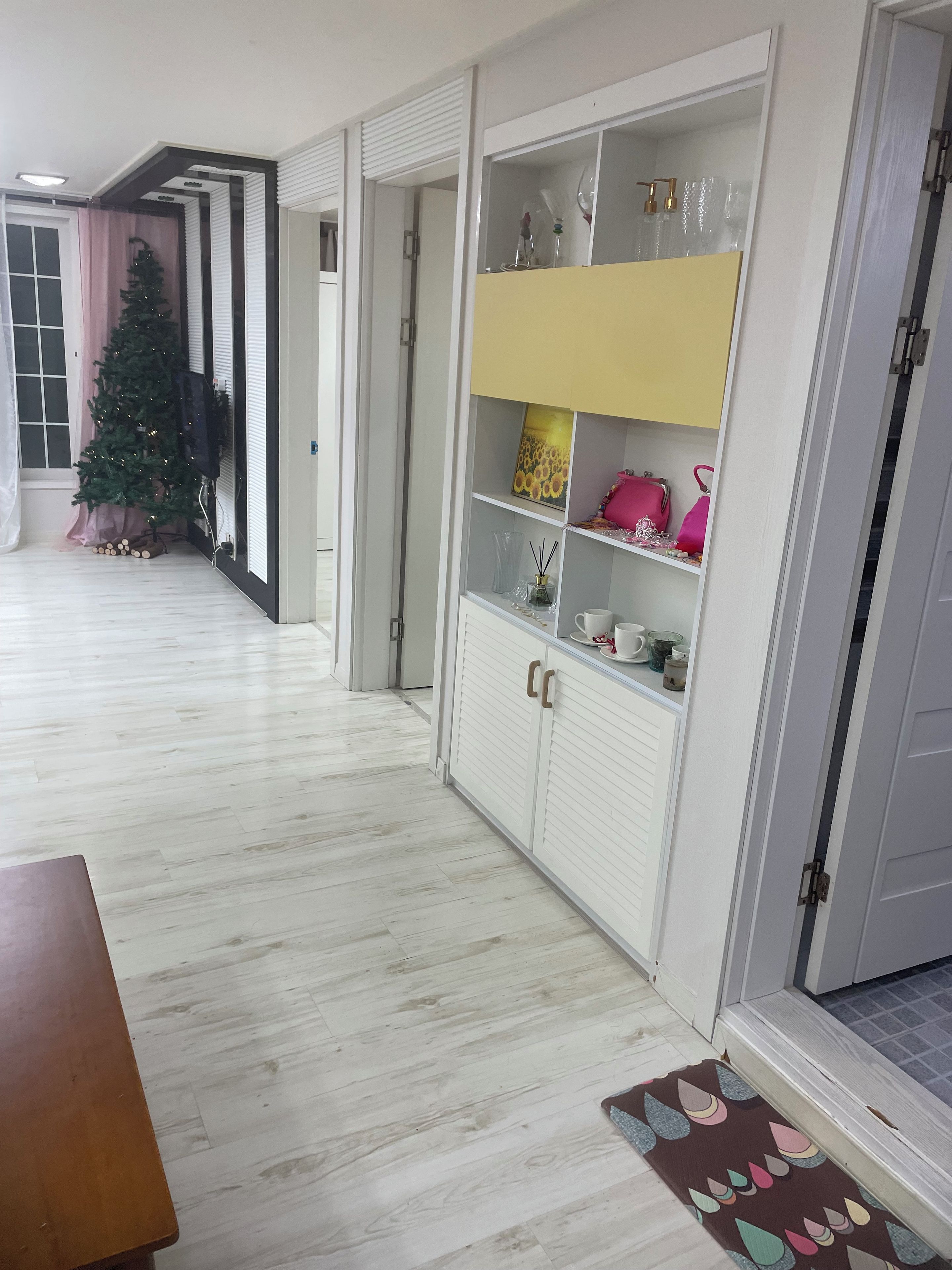 Un pasillo con un árbol de Navidad, un armario blanco con estantes y una alfombra estampada.