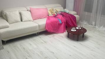 A living room with a white sofa, a pink blanket, a small wooden side table with a cup and saucer, and a large air conditioning unit on the wall.