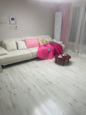 A living room with a white sofa, a pink blanket, a small wooden side table with a cup and saucer, and a large air conditioning unit on the wall. - Lucky Guesthouse (Non-Korean Nationals Women only) (Incheon)