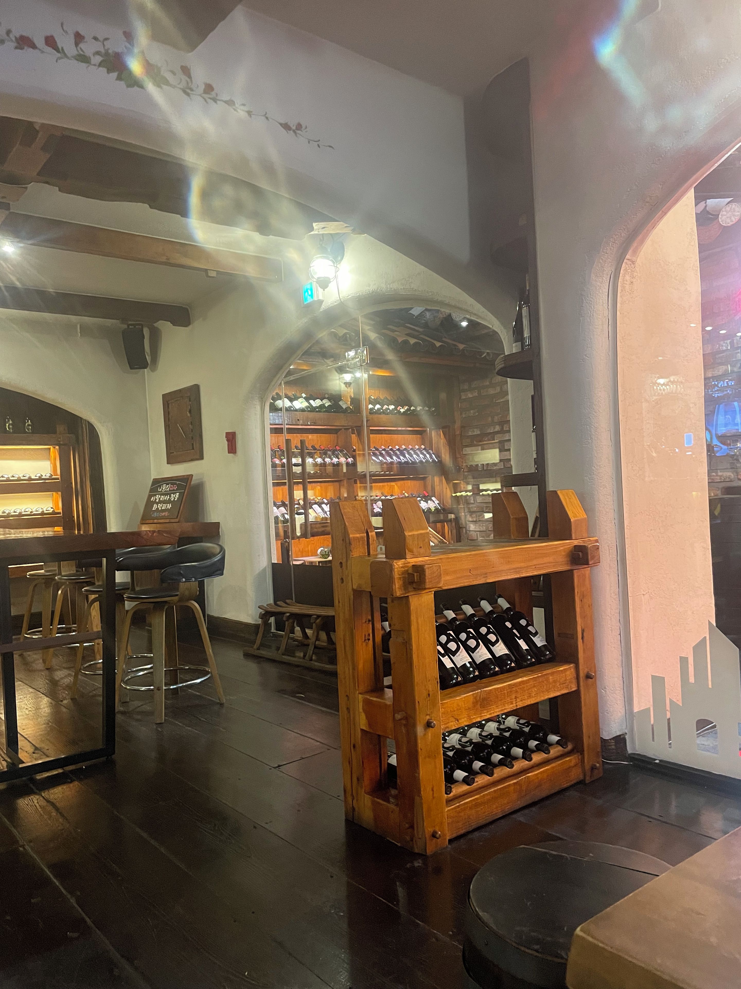 A bar area with wooden stools, a wine rack, and a wooden display case.