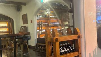 A bar area with wooden stools, a wine rack, and a wooden display case.