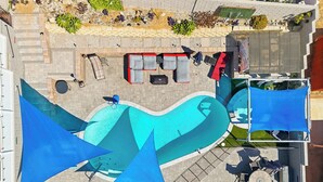 Eine Luftaufnahme eines Poolbereichs auf einem Dach mit Pool, Liegestühlen, einem Tisch mit Stühlen und einer überdachten Sitzgruppe.